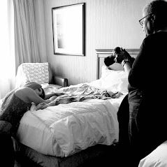 A photographer captures a black and white shot of a person resting on a hotel bed.