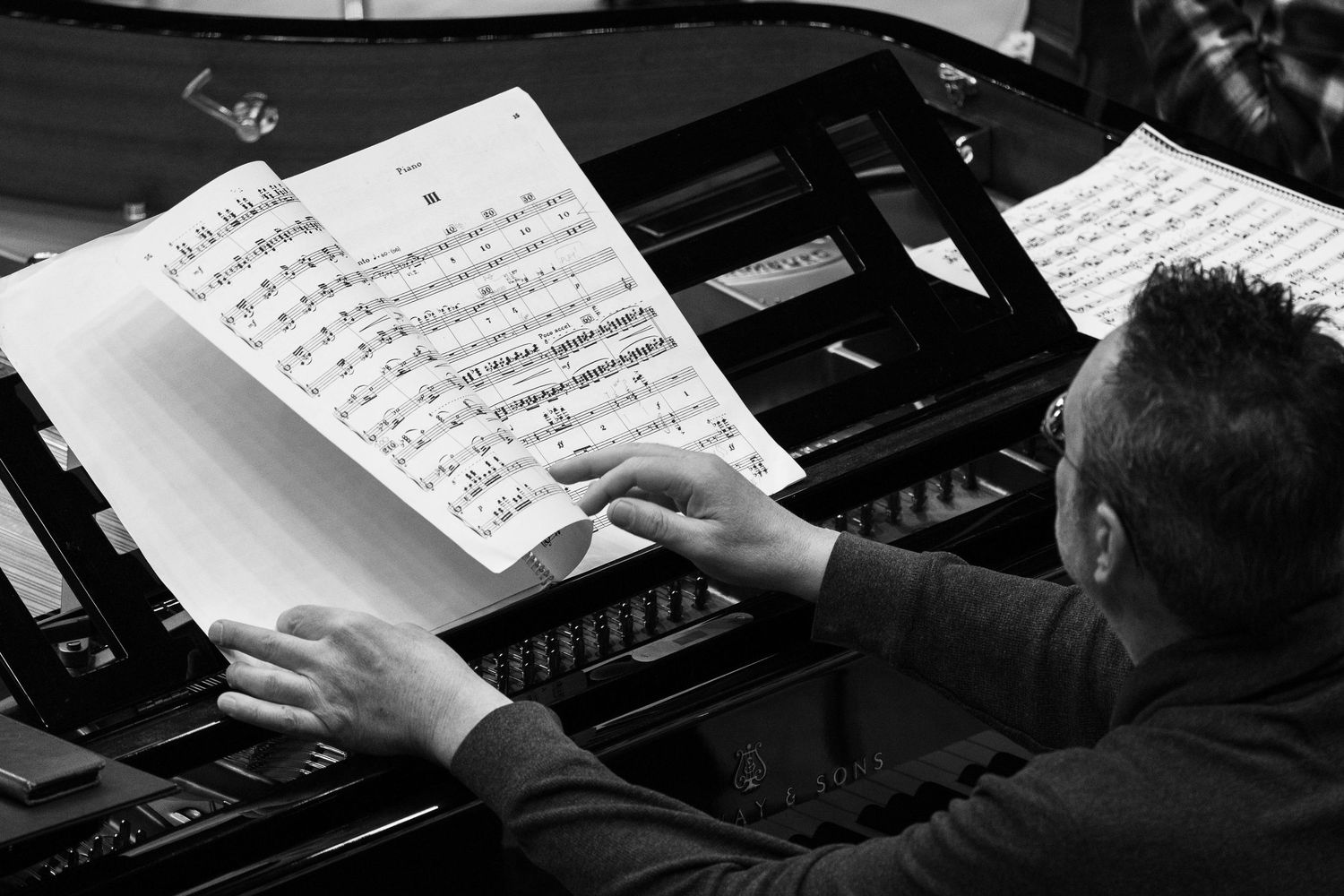 A pianist's hands rest on piano keys while reading sheet music in black and white.