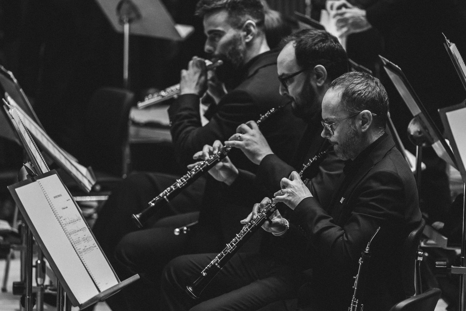 Black and white photo of musicians playing clarinets in an orchestra concert performance.