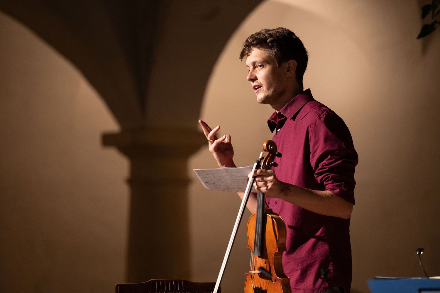 Violinist performing in dramatic spotlight against warm brown background.