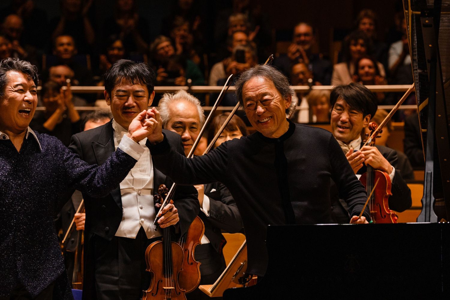Musicians and conductor bow on stage at a concert hall, smiling after a classical orchestra performance.