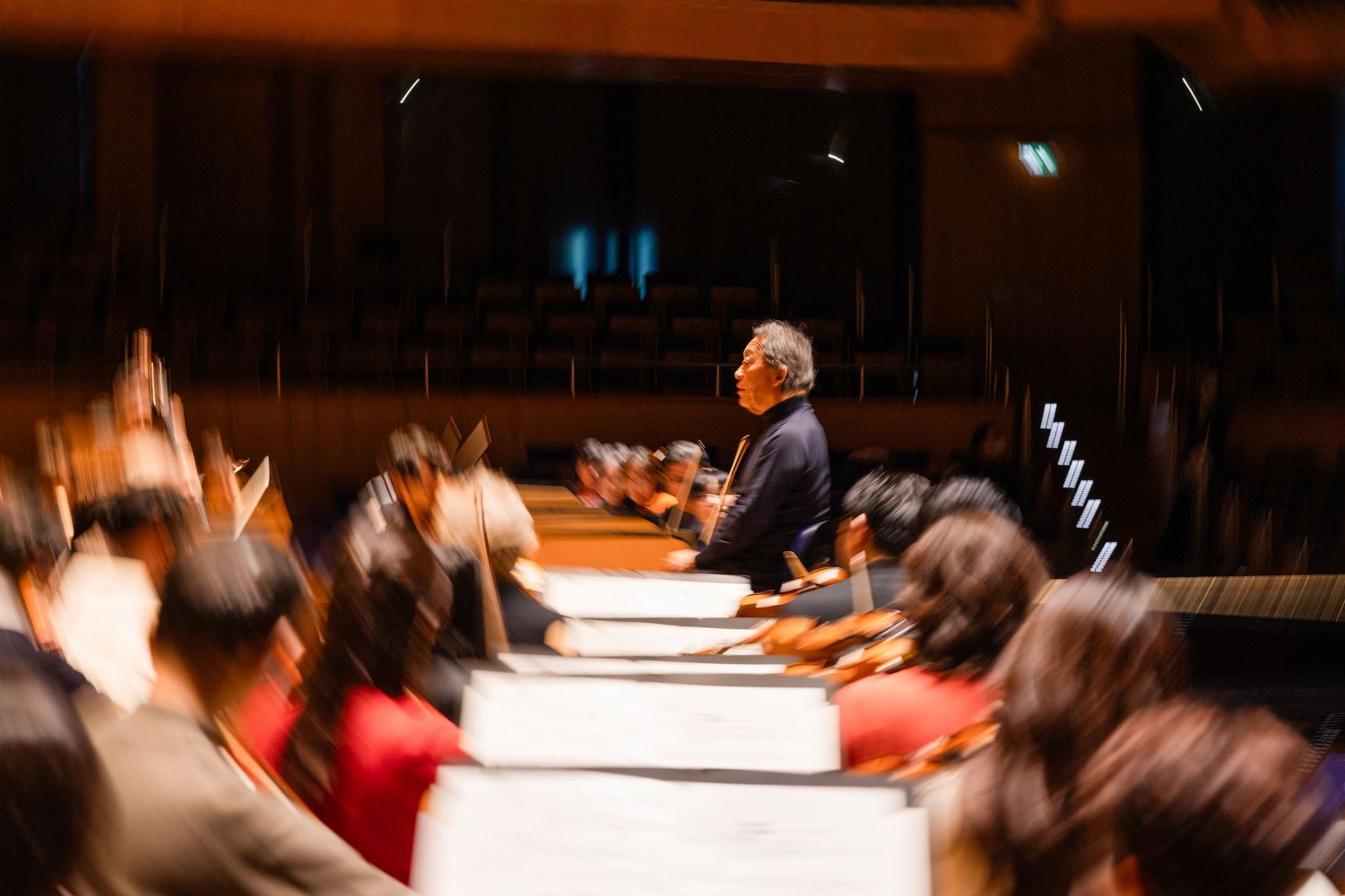 Orchestra conductor leading musicians during a rehearsal in a concert hall with blurred motion effect.
