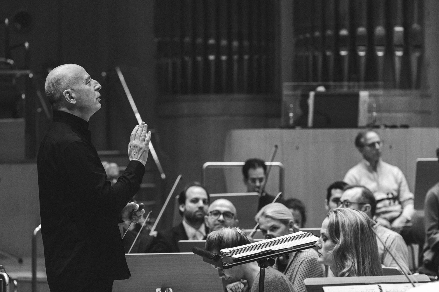 Black and white photo of an orchestra conductor leading musicians during a classical performance rehearsal.