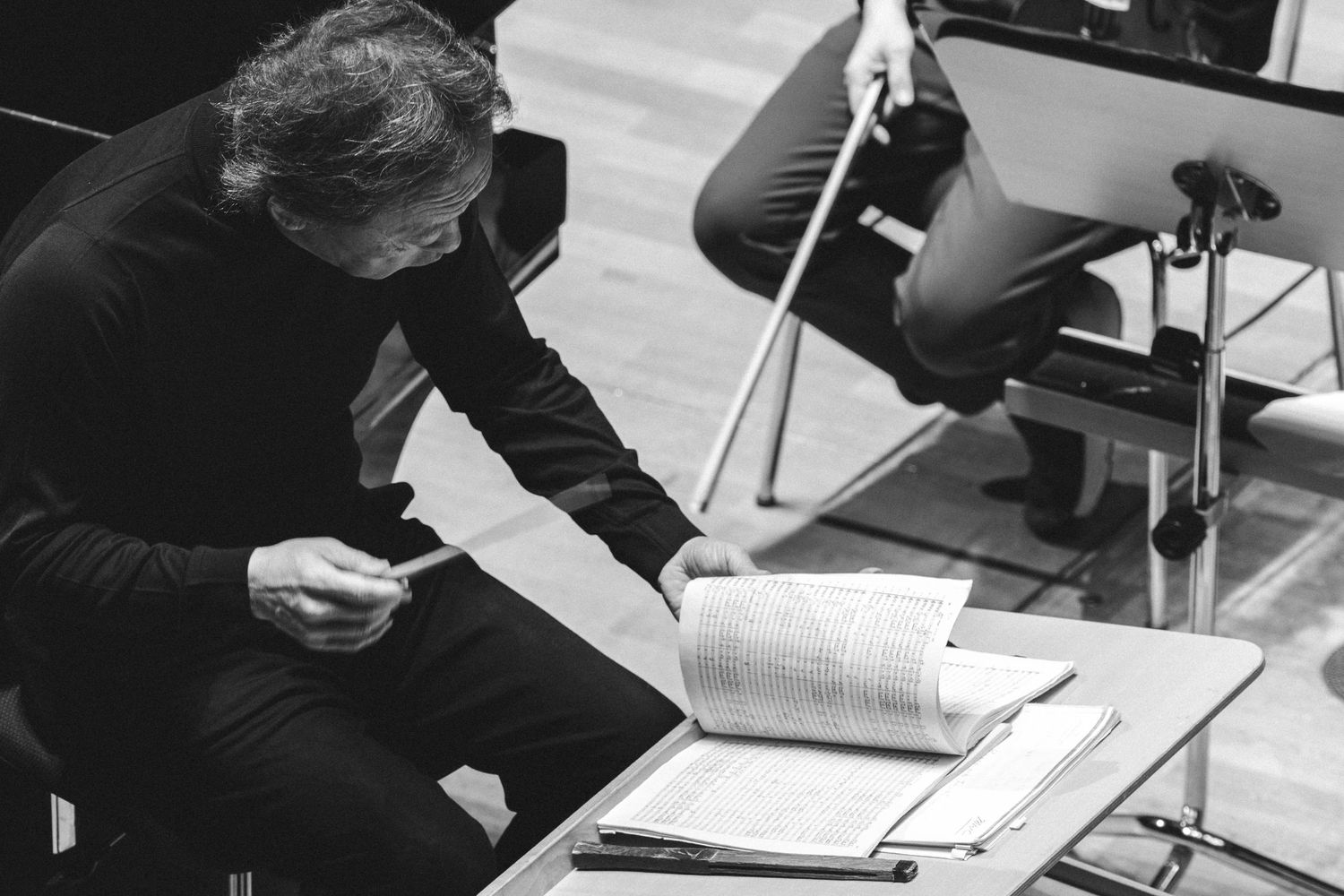 Musician reviews sheet music at a stand during an orchestra rehearsal in black and white photography.