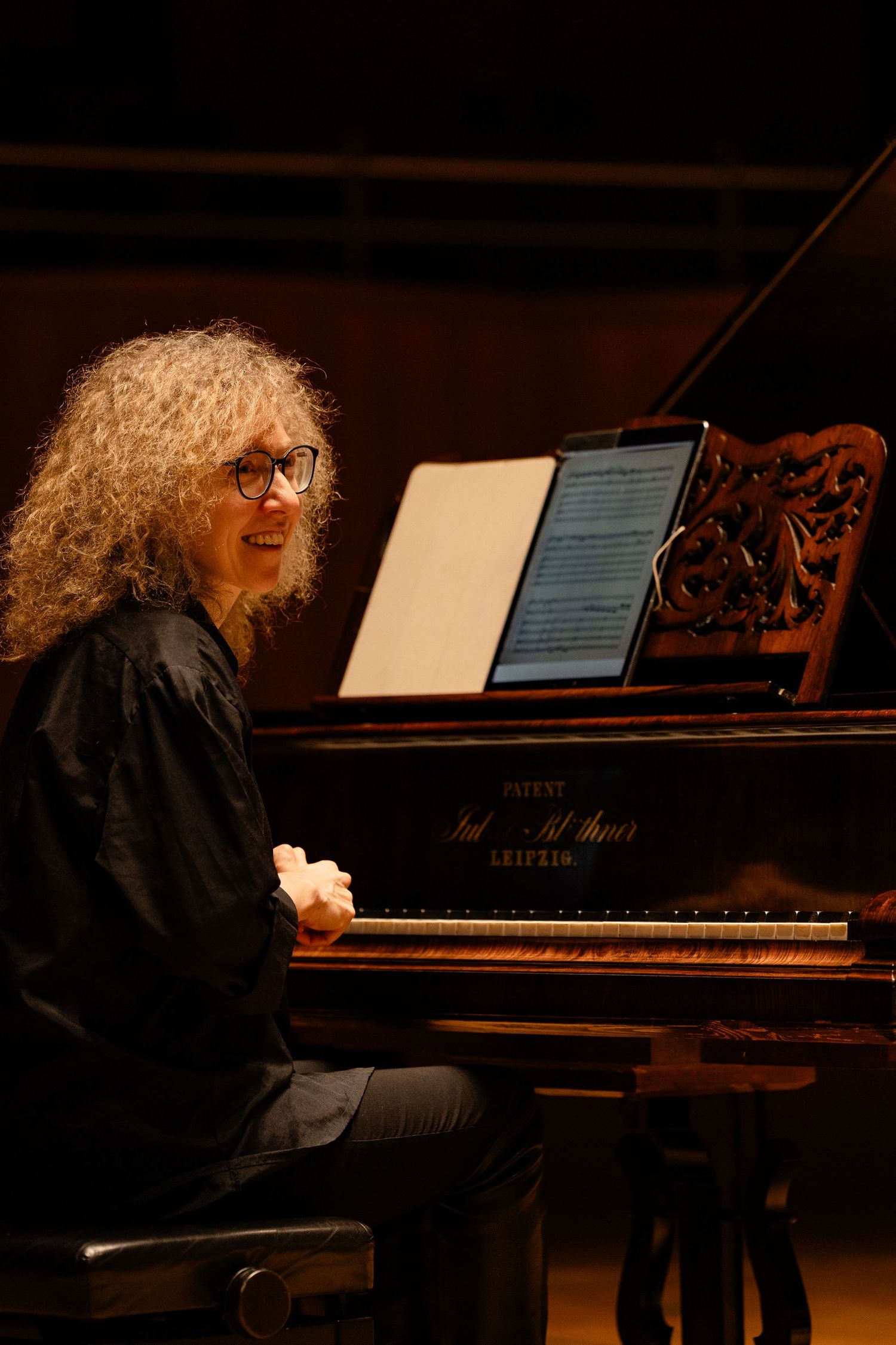 Curly-haired pianist with glasses performing on a grand piano, reading sheet music during a concert.