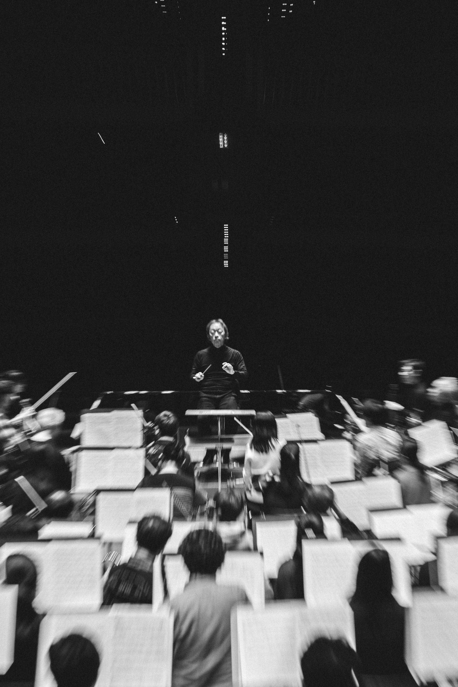 Orchestra conductor leads musicians in dramatic black and white performance photography shot from above.