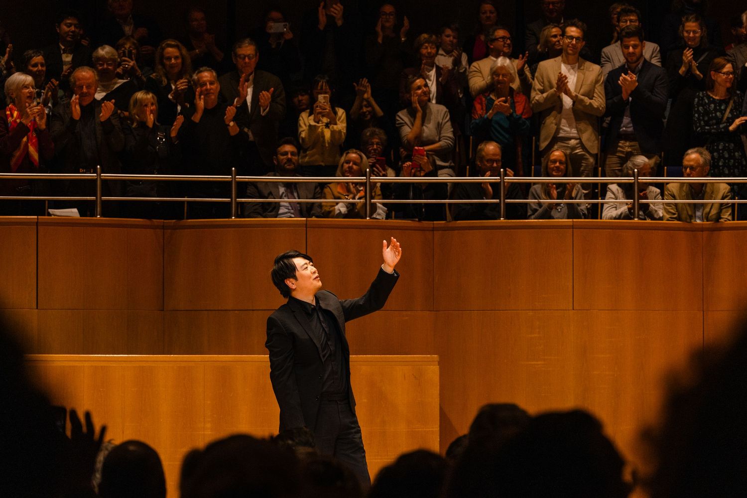 Conductor bows on stage before applauding audience in a warmly lit concert hall.