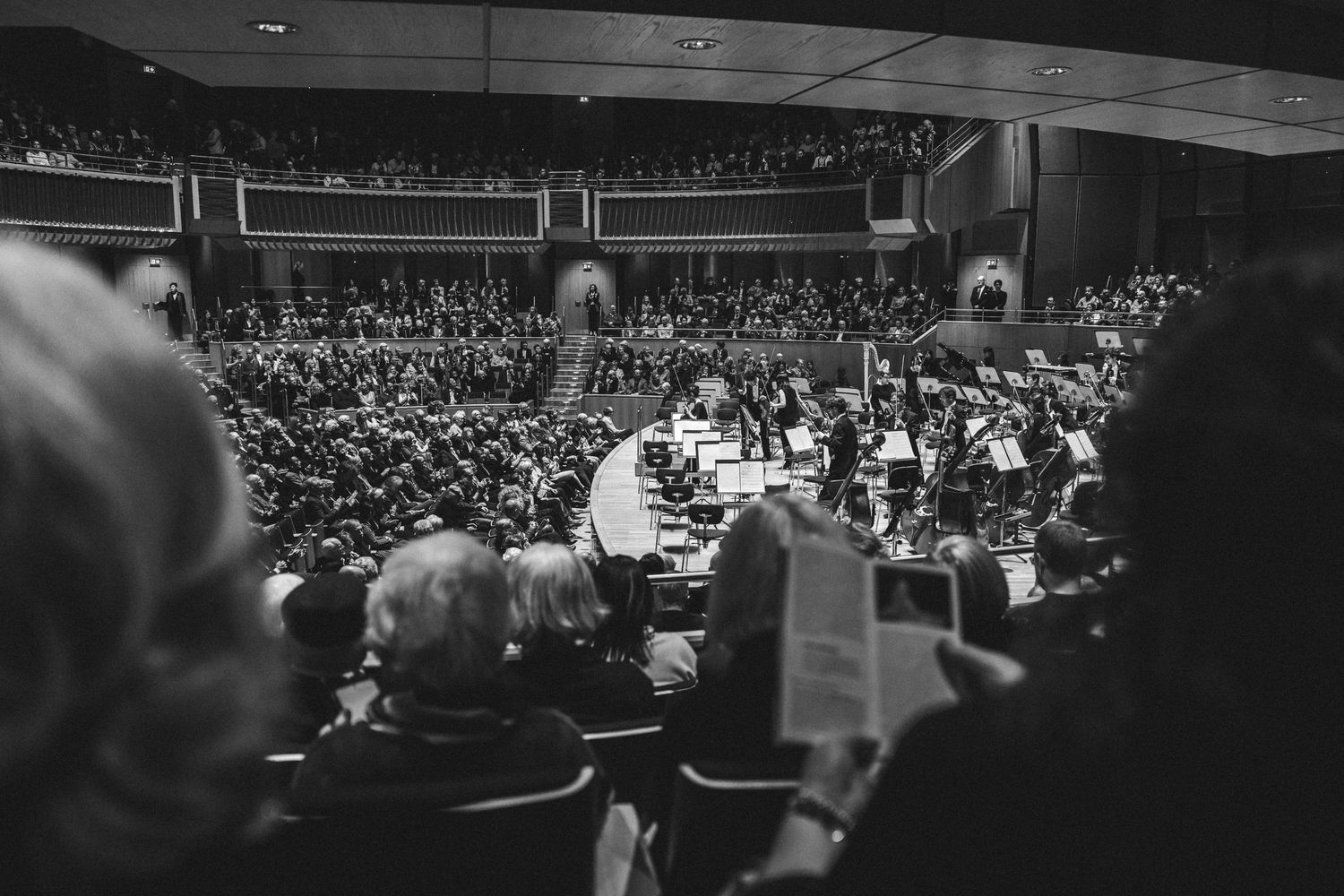 Black and white photo of a packed concert hall with a full orchestra performing on stage.