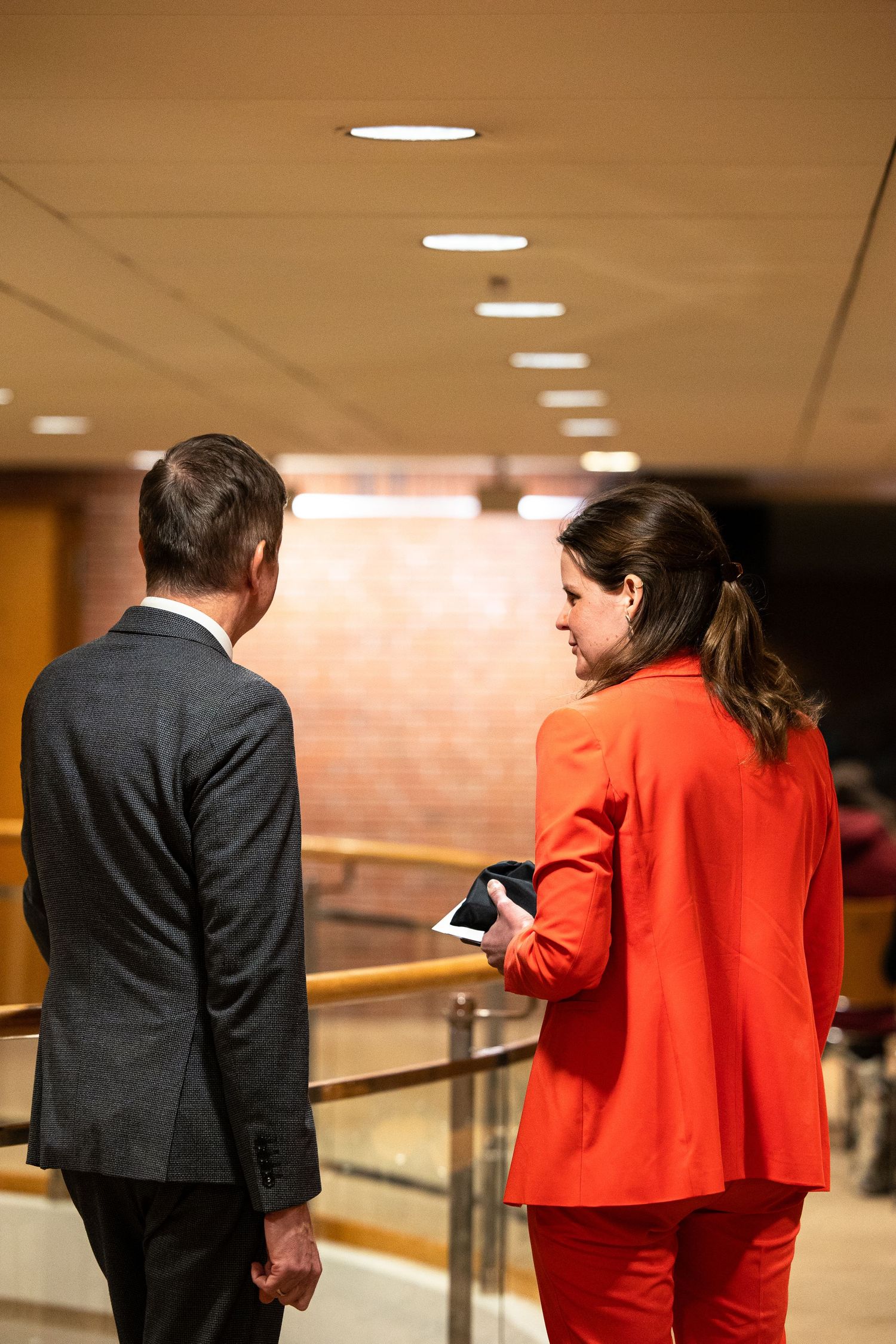 Two business professionals in formal attire reviewing a tablet device in a modern office corridor.