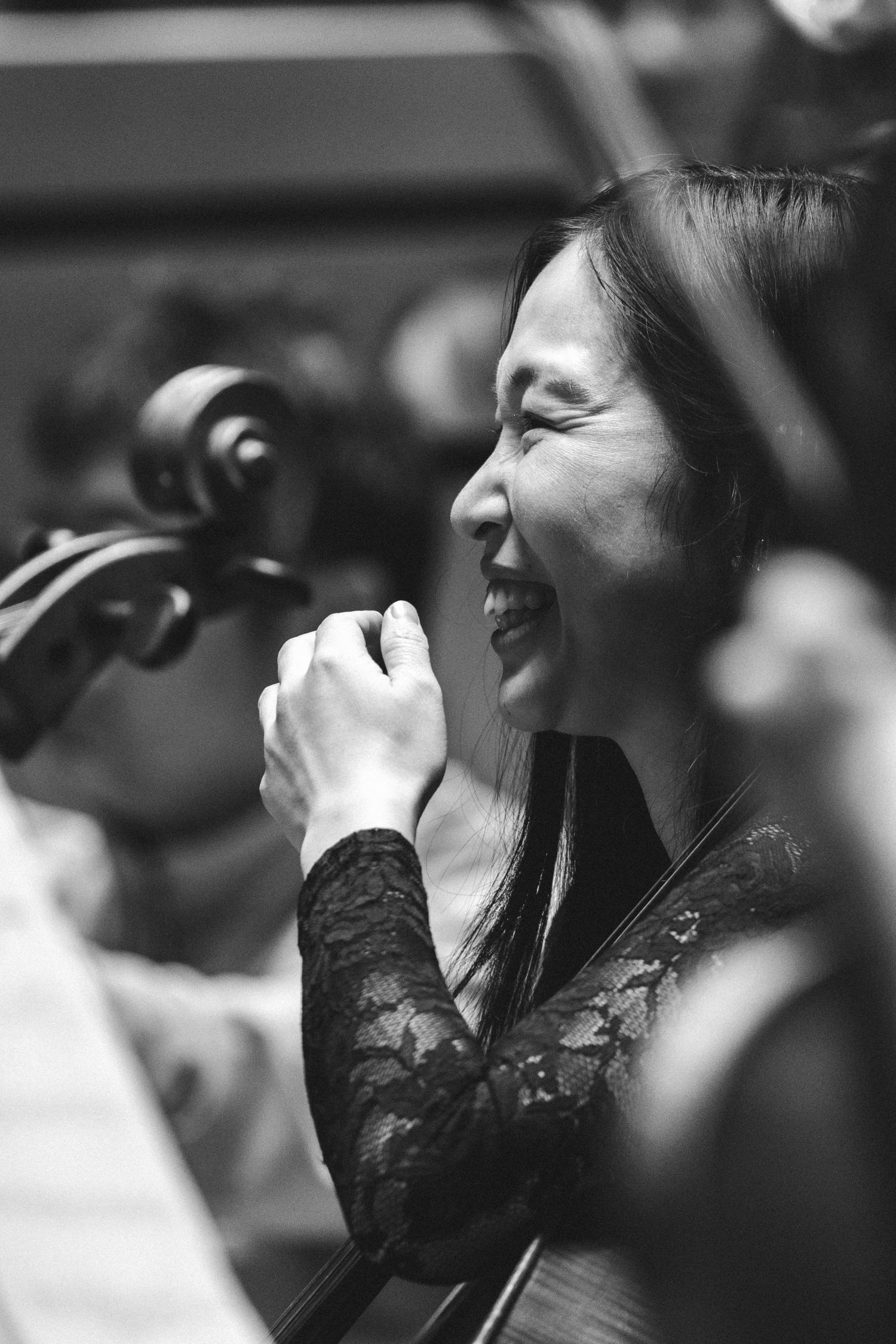 Smiling Asian woman musician holding a violin, black and white photo in an orchestra setting.