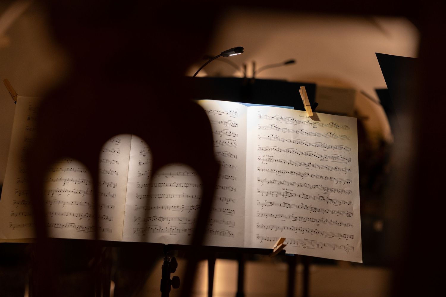 Sheet music on a music stand illuminated by a small lamp during an orchestra rehearsal or performance.