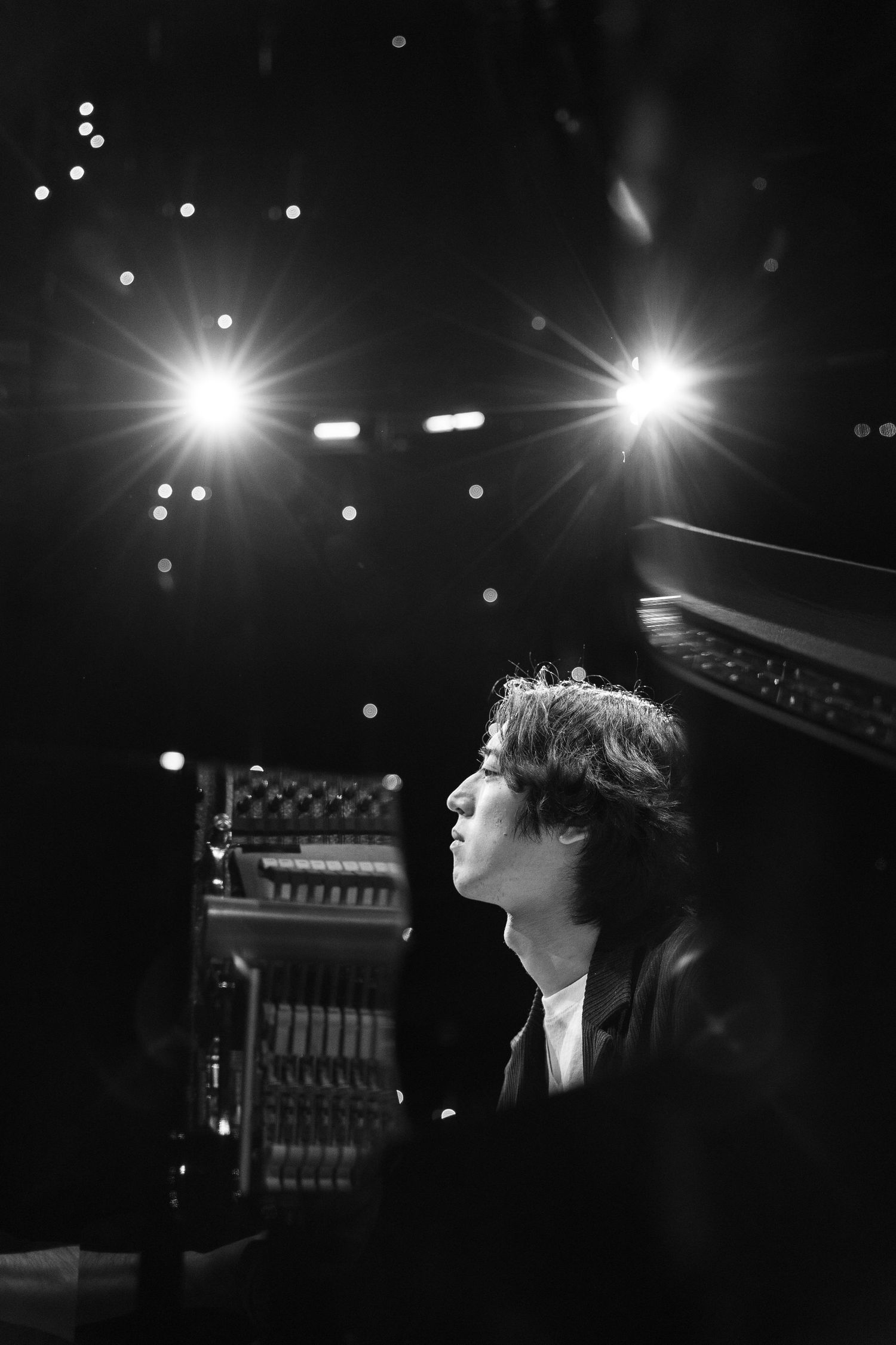 Black and white photo of a young musician gazing upward under bright stage lights during a live performance.