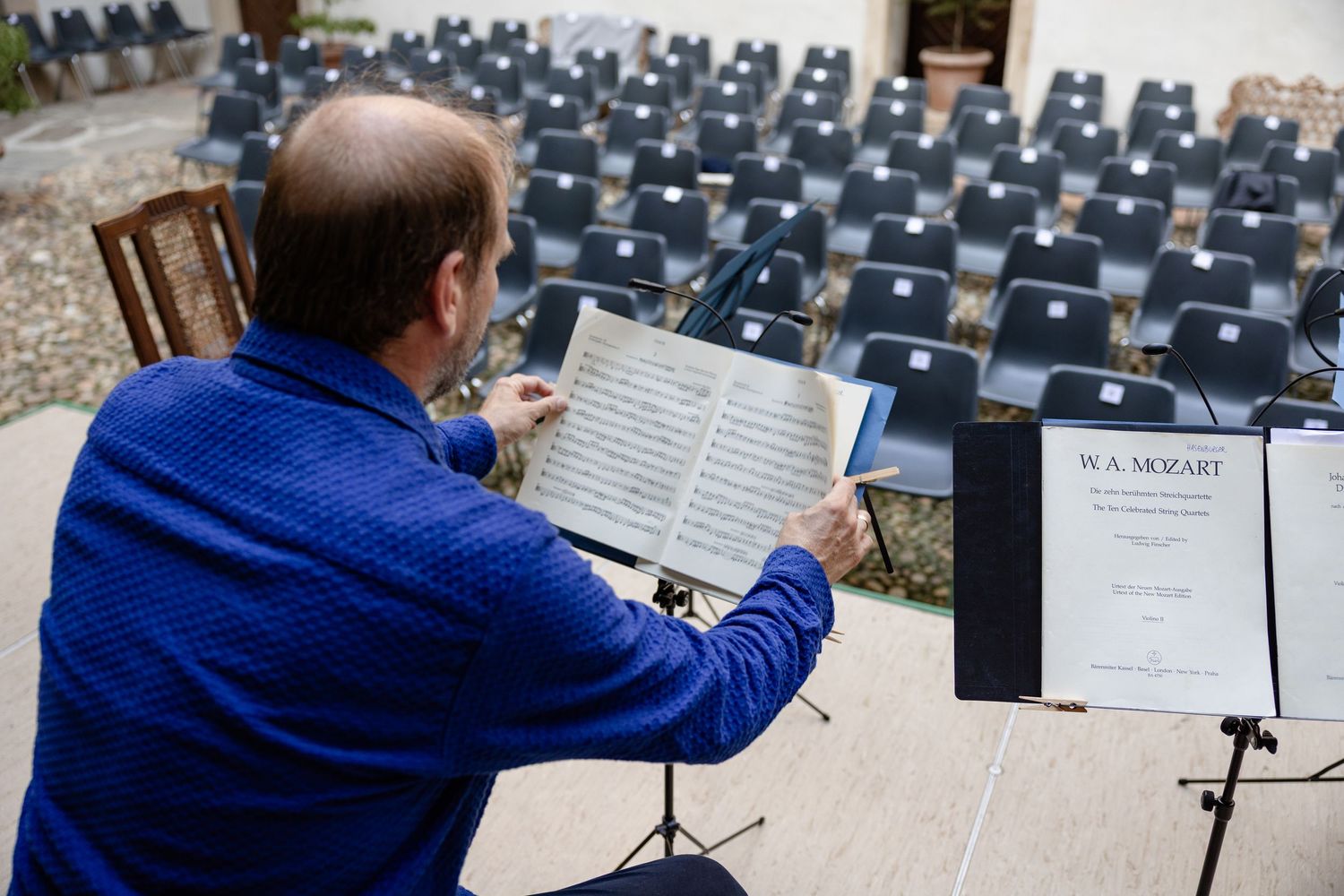 Musician reviews W.A. Mozart sheet music on a stand before an outdoor concert with empty chairs.