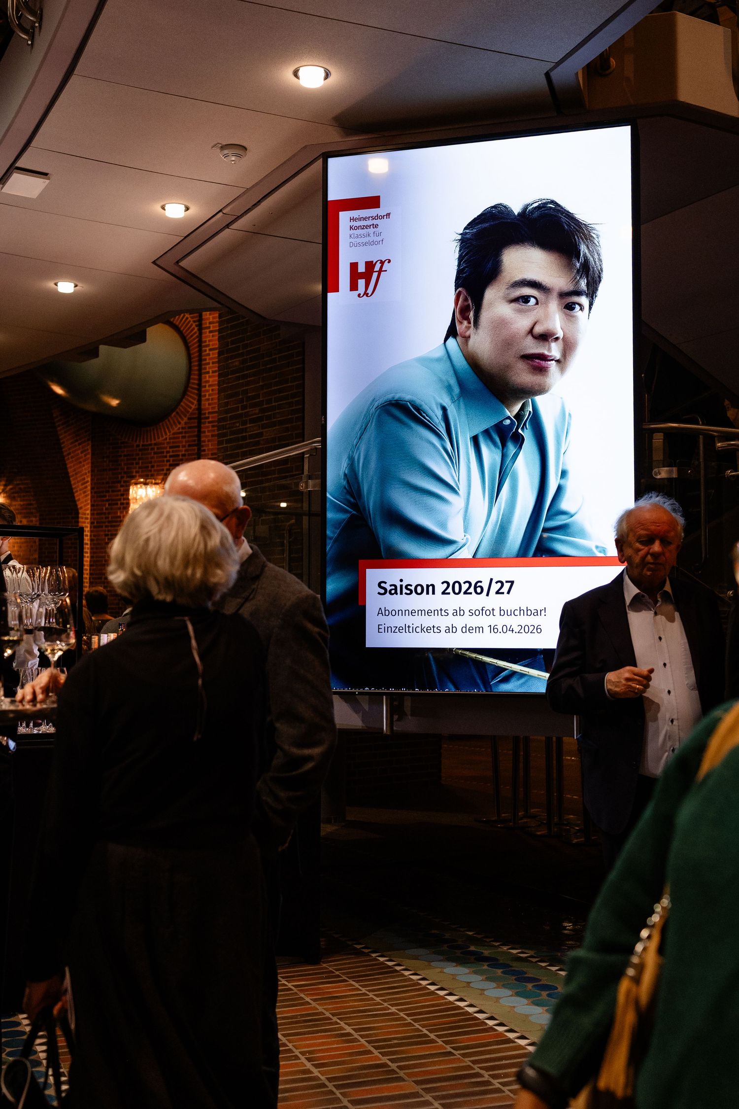 Digital billboard displaying Saison 2026/27 concert season advertisement featuring an Asian male pianist at a venue entrance.