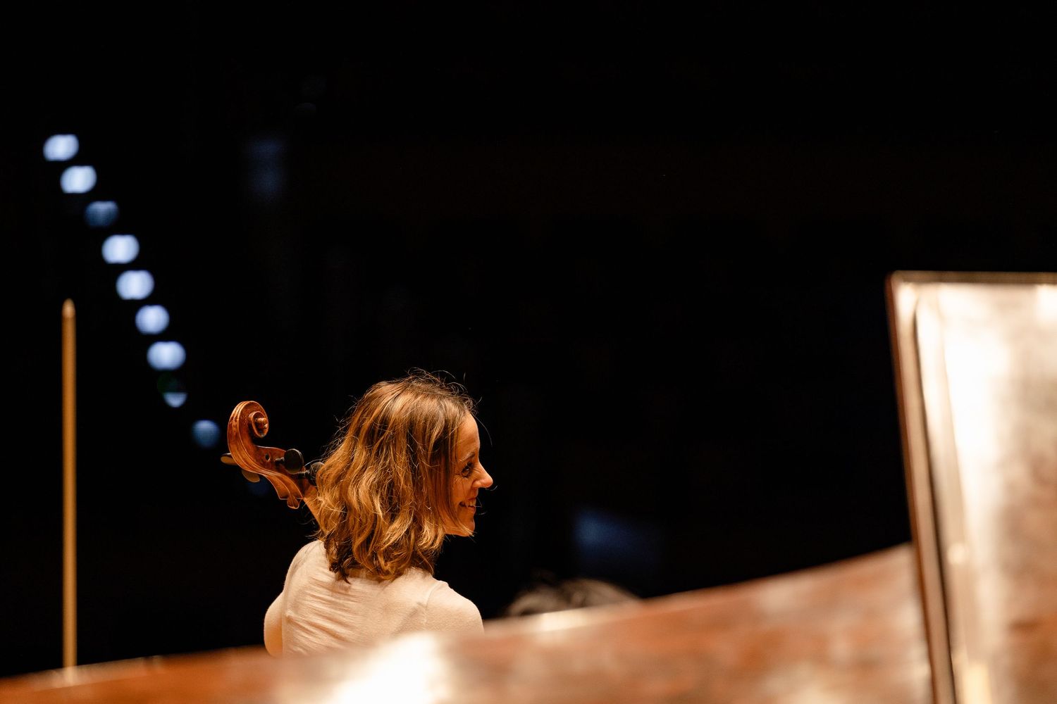 Female cellist performing on stage in a dimly lit concert hall, captured in profile view.