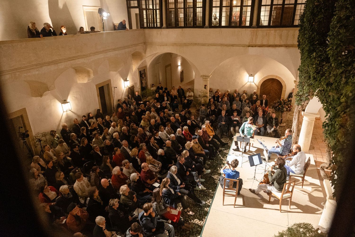 Large audience gathered in an elegant courtyard venue for an intimate chamber music concert at night.