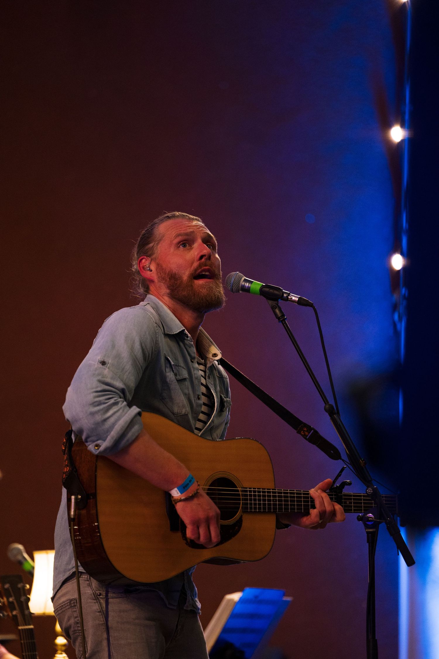 Musician performs passionately on acoustic guitar under dramatic blue stage lighting during live concert performance.