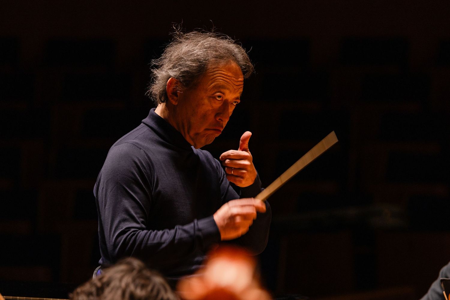 Orchestra conductor leading a performance, holding a baton with expressive gestures in a dark concert hall.