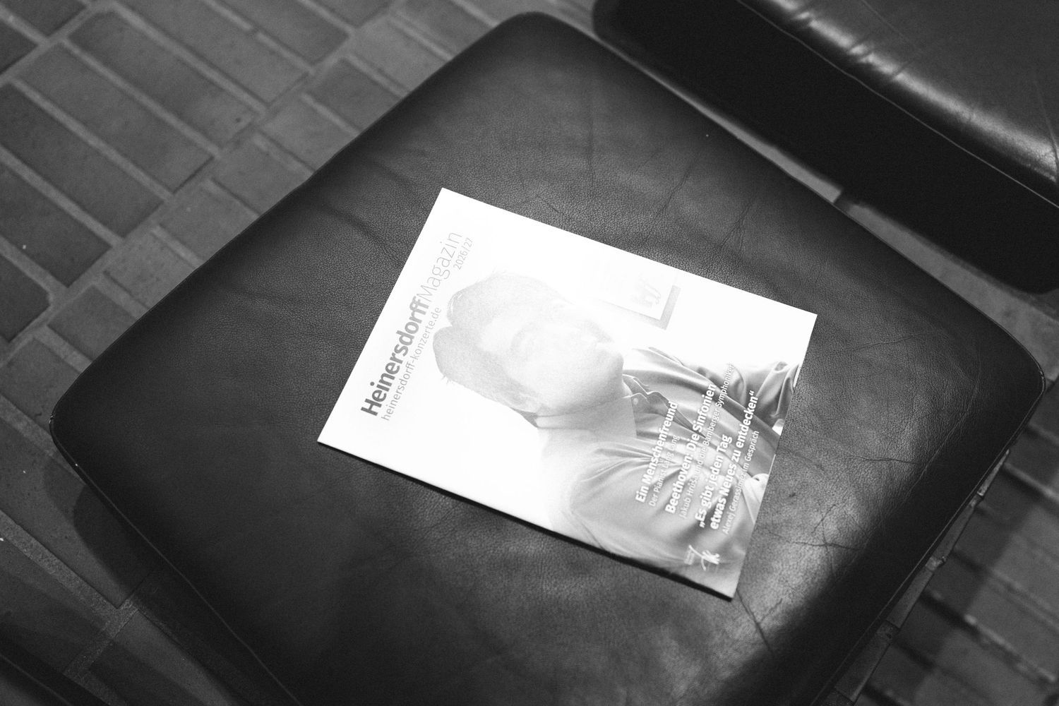 Black and white photo of a magazine resting on a leather ottoman in a modern interior setting.