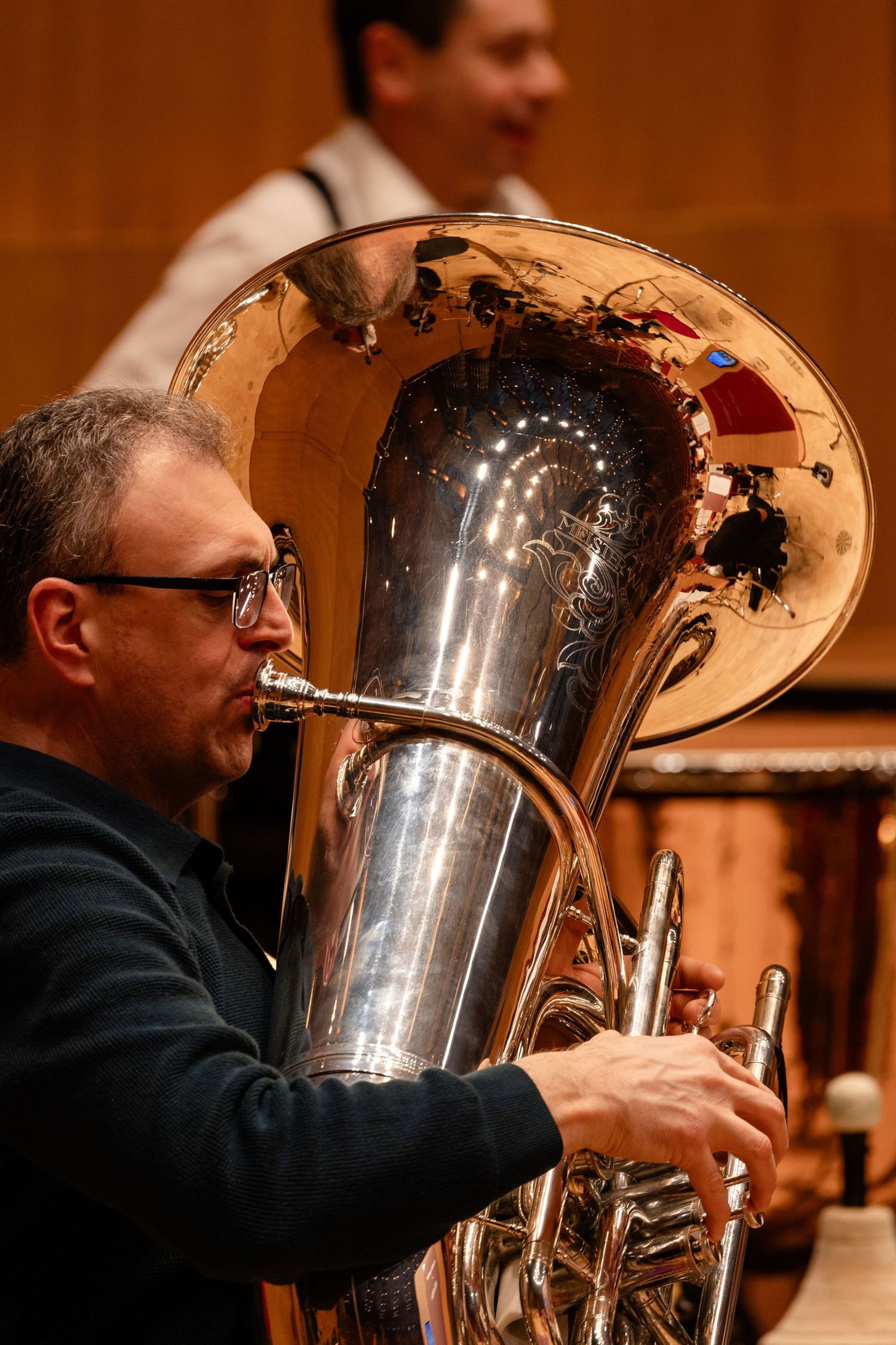 Musician playing a tuba in a concert hall, with a reflection visible in the brass instrument's bell.