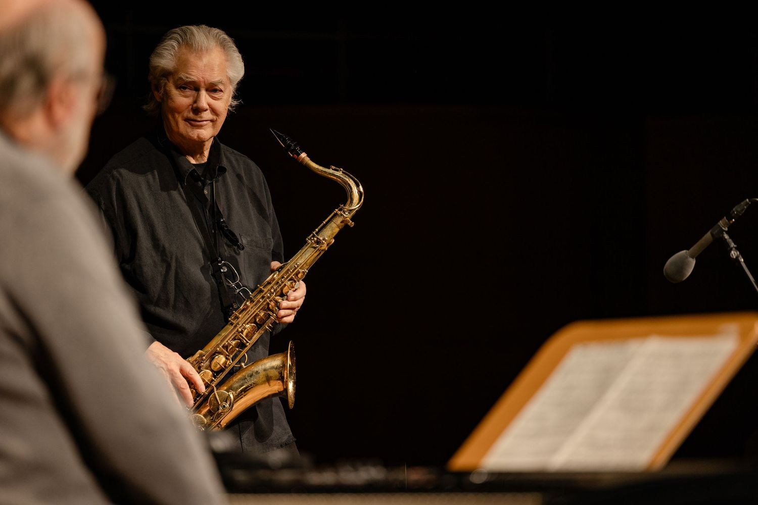 Jazz musician playing a golden saxophone on stage under dramatic lighting during a live performance.