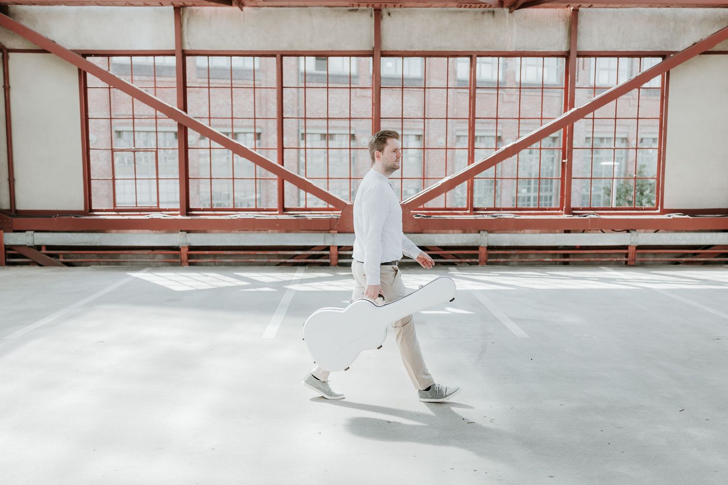 Person in white outfit walking through a spacious industrial building with red steel frame windows.