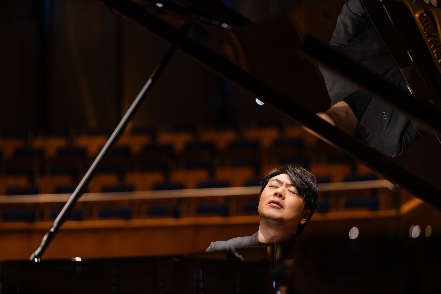 A pianist performs passionately at a grand piano on a concert hall stage, eyes closed in musical expression.