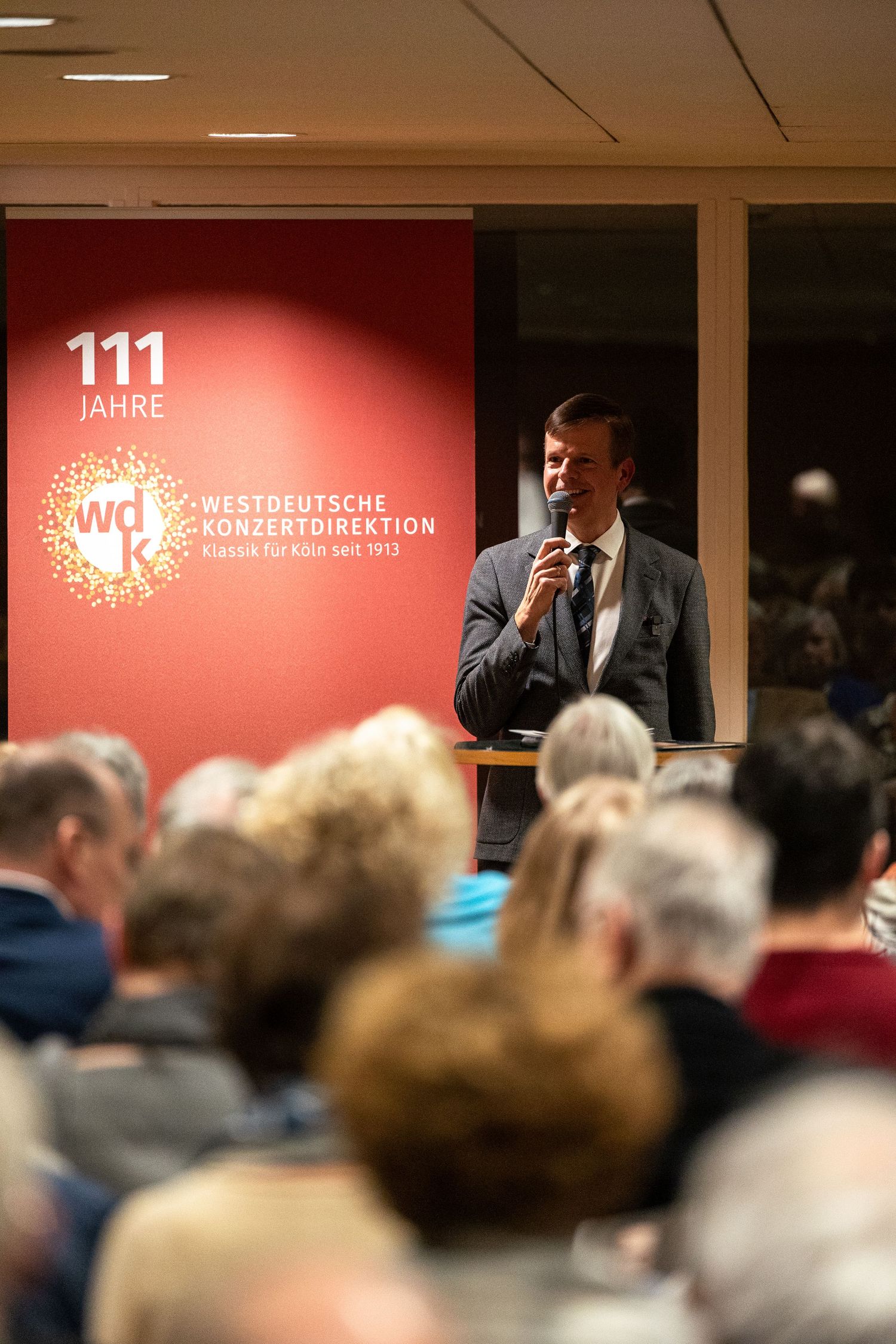 A speaker addresses an audience at the 111th anniversary event of Westdeutsche Konzertdirektion in Cologne.