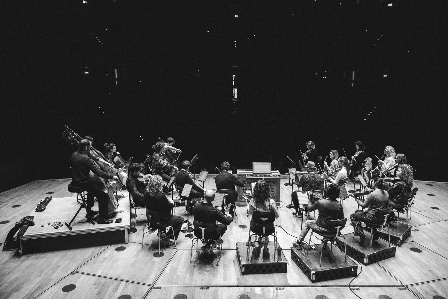 Black and white photo of an orchestra rehearsing on a wooden stage in a concert hall.