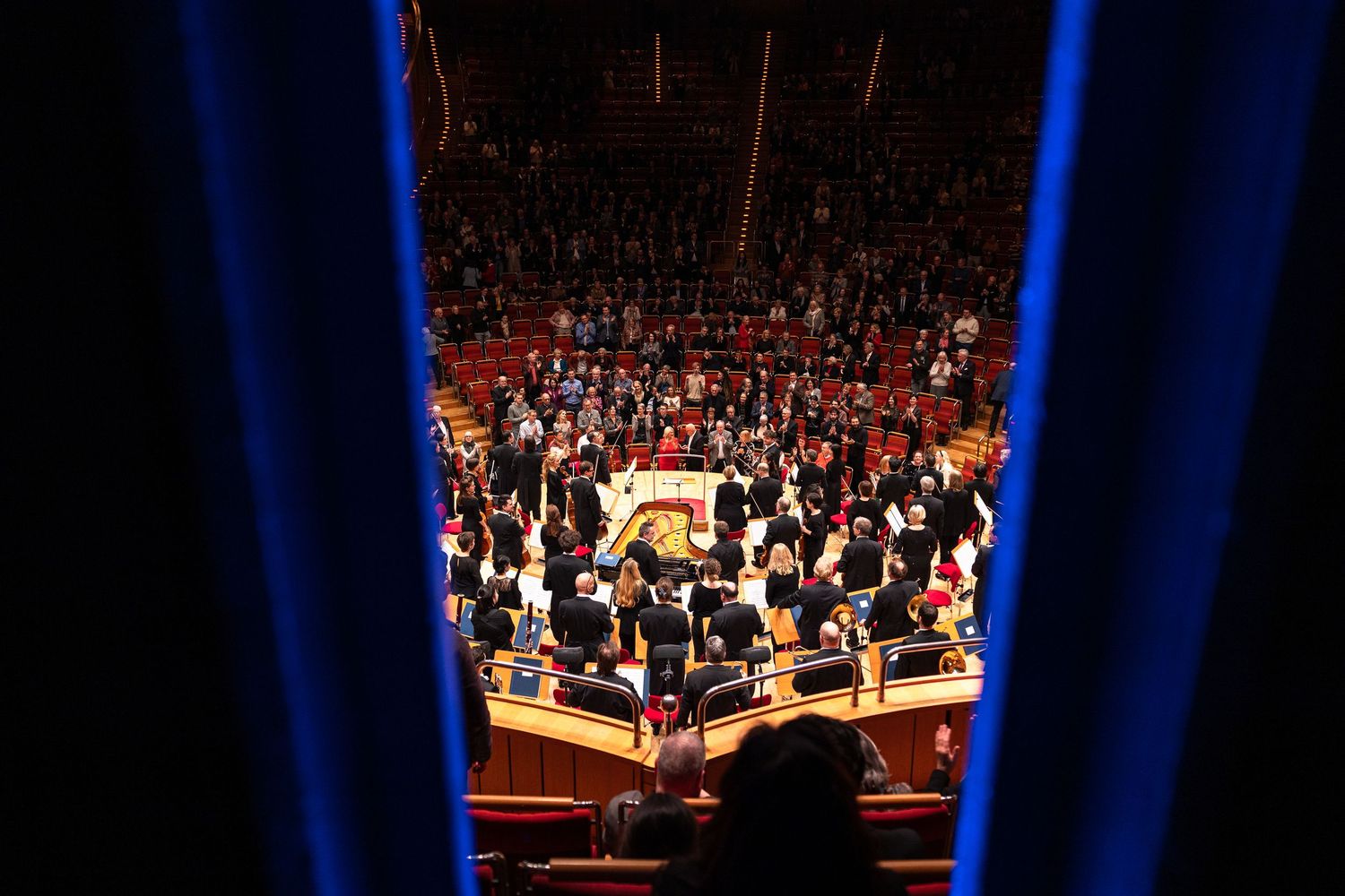 Aerial view of a packed legislative chamber with blue curtains framing crowds of people gathered on the floor.