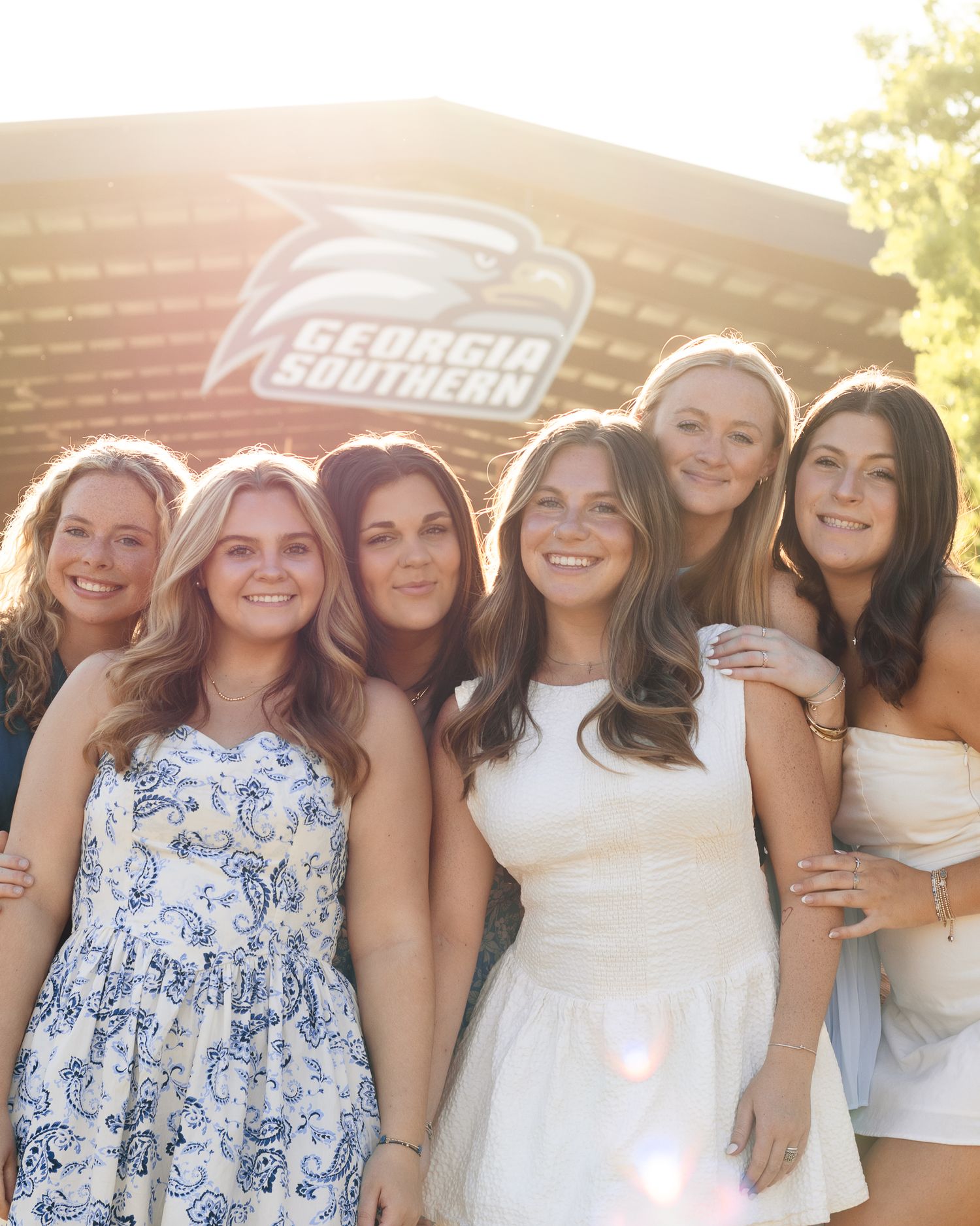Six smiling young women pose close together outdoors in warm sunlight in front of a Georgia Southern University eagle logo sign.
