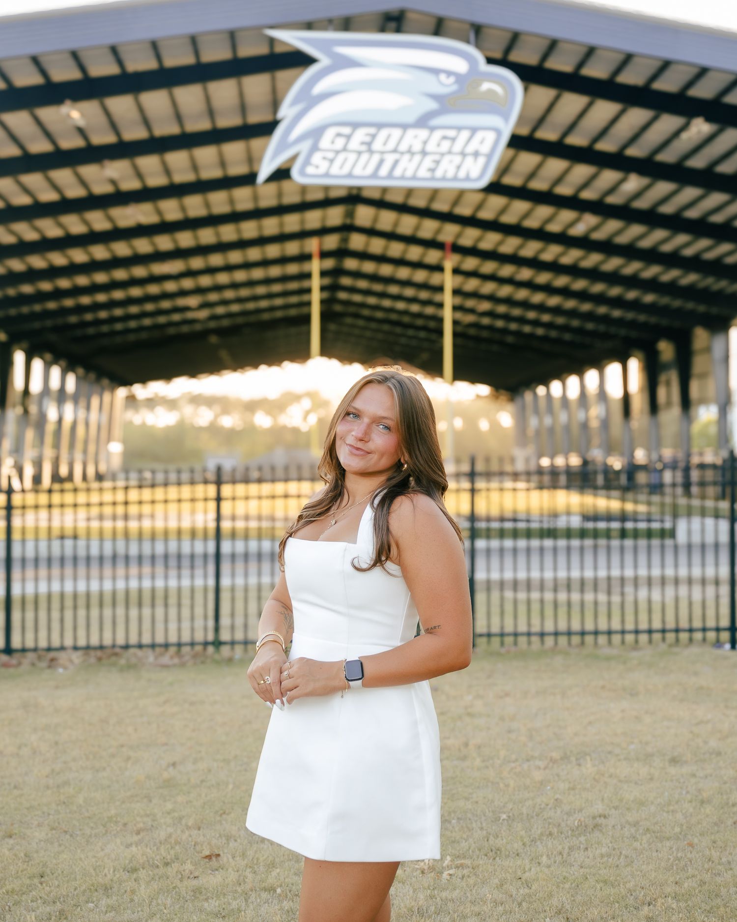 Smiling young woman in a white dress poses on a grassy lawn beneath a covered pavilion with a Georgia Southern Eagles logo sign.