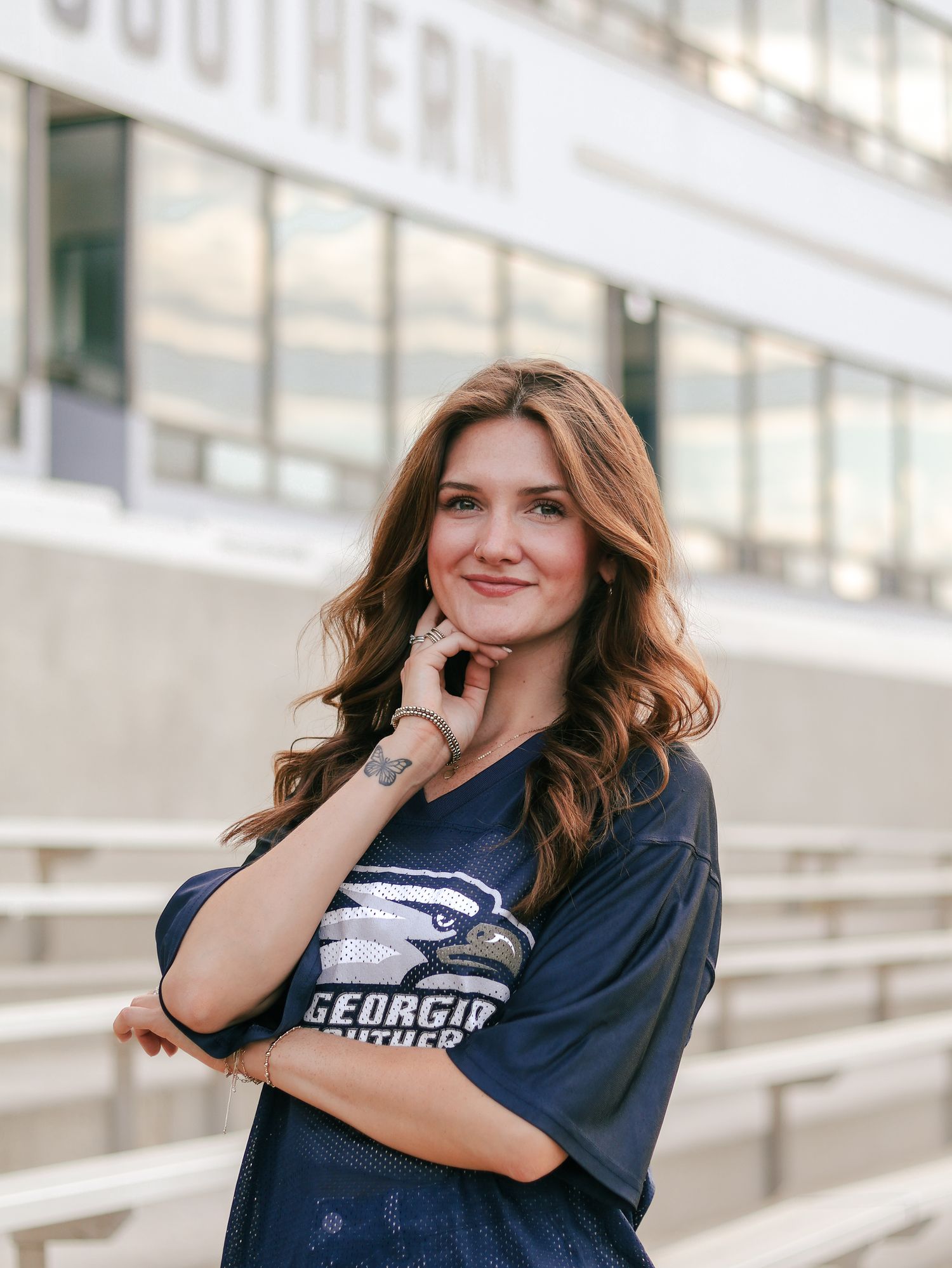 Smiling woman with long auburn hair wears a navy Georgia Southern football jersey while posing on empty stadium bleachers.
