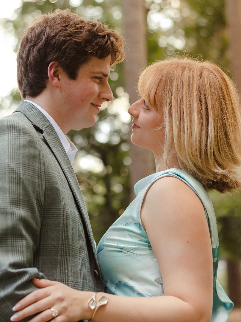 A man in a gray plaid blazer gazes lovingly at a woman in a teal dress during an outdoor engagement session.