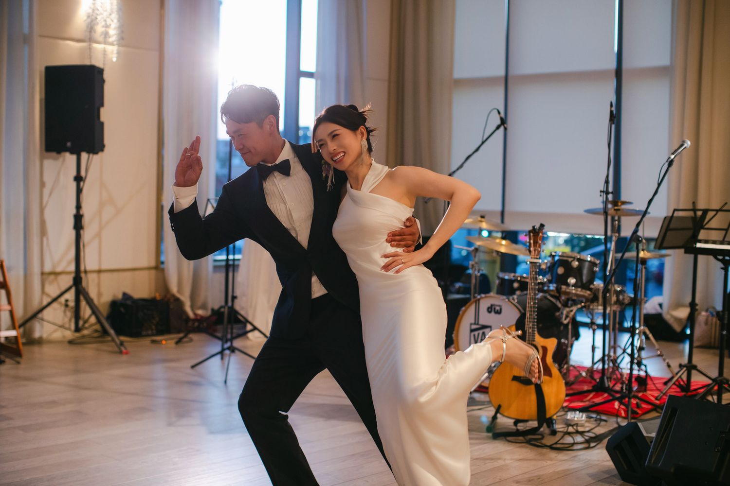 Bride and groom strike a fun dance pose together during their wedding reception with a live band stage behind them.