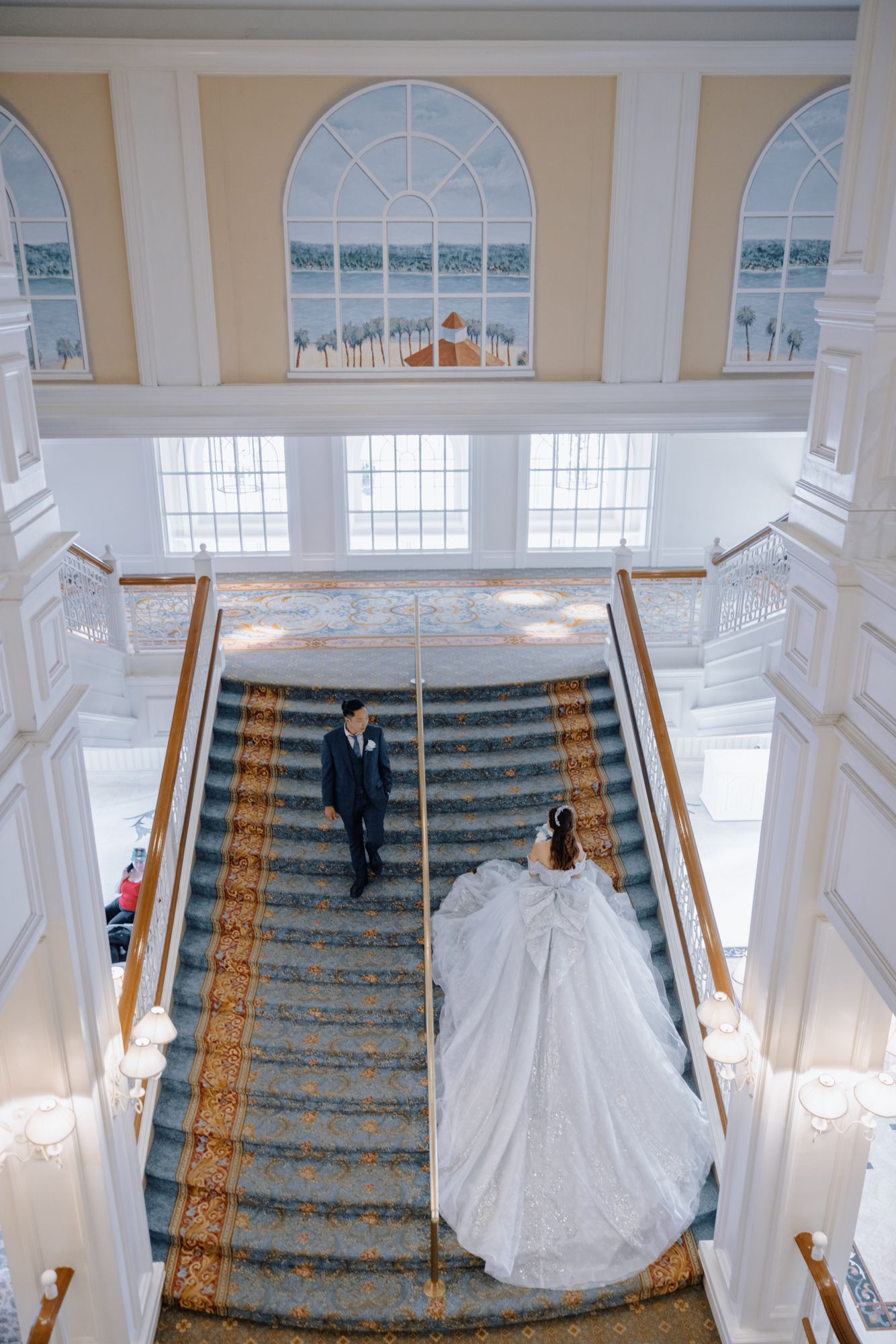 Bride and groom share romantic moment on ornate carpeted grand staircase in elegant venue.