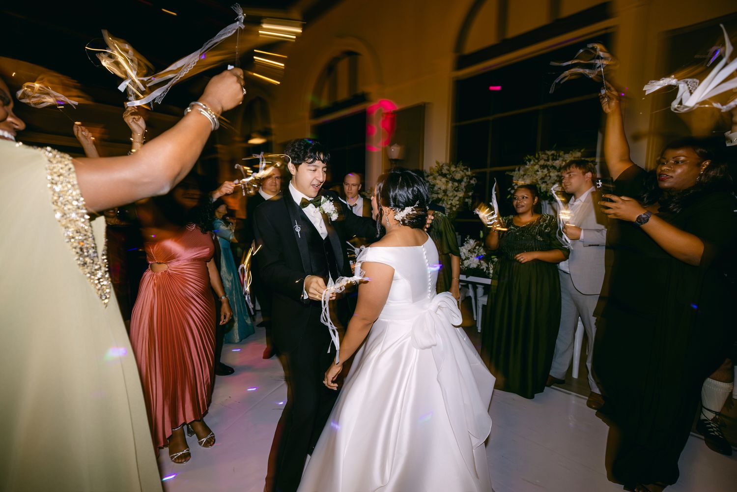 Bride and groom dance while joyful guests wave sparklers and decorative fans at their lively wedding reception.