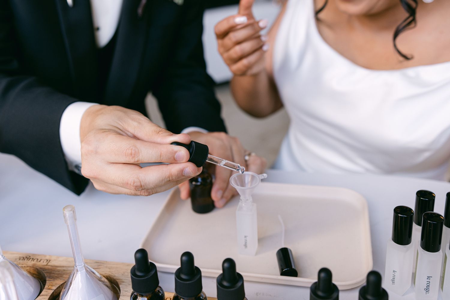Couple in wedding attire blend custom fragrance oils with glass droppers and small bottles at a wedding perfume ceremony.