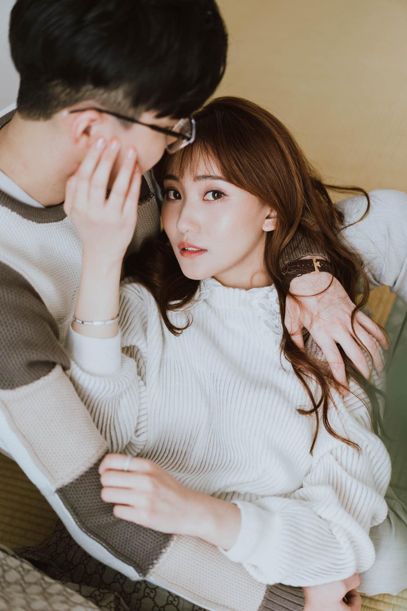Young Asian couple sharing an intimate moment on a cozy chair indoors.