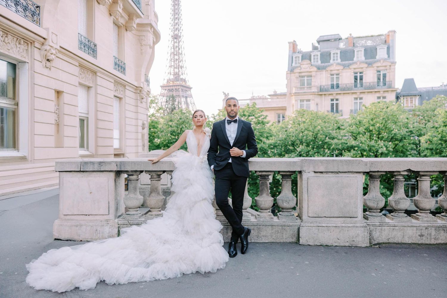Bride and groom pose elegantly on stone terrace with Eiffel Tower in background Paris.