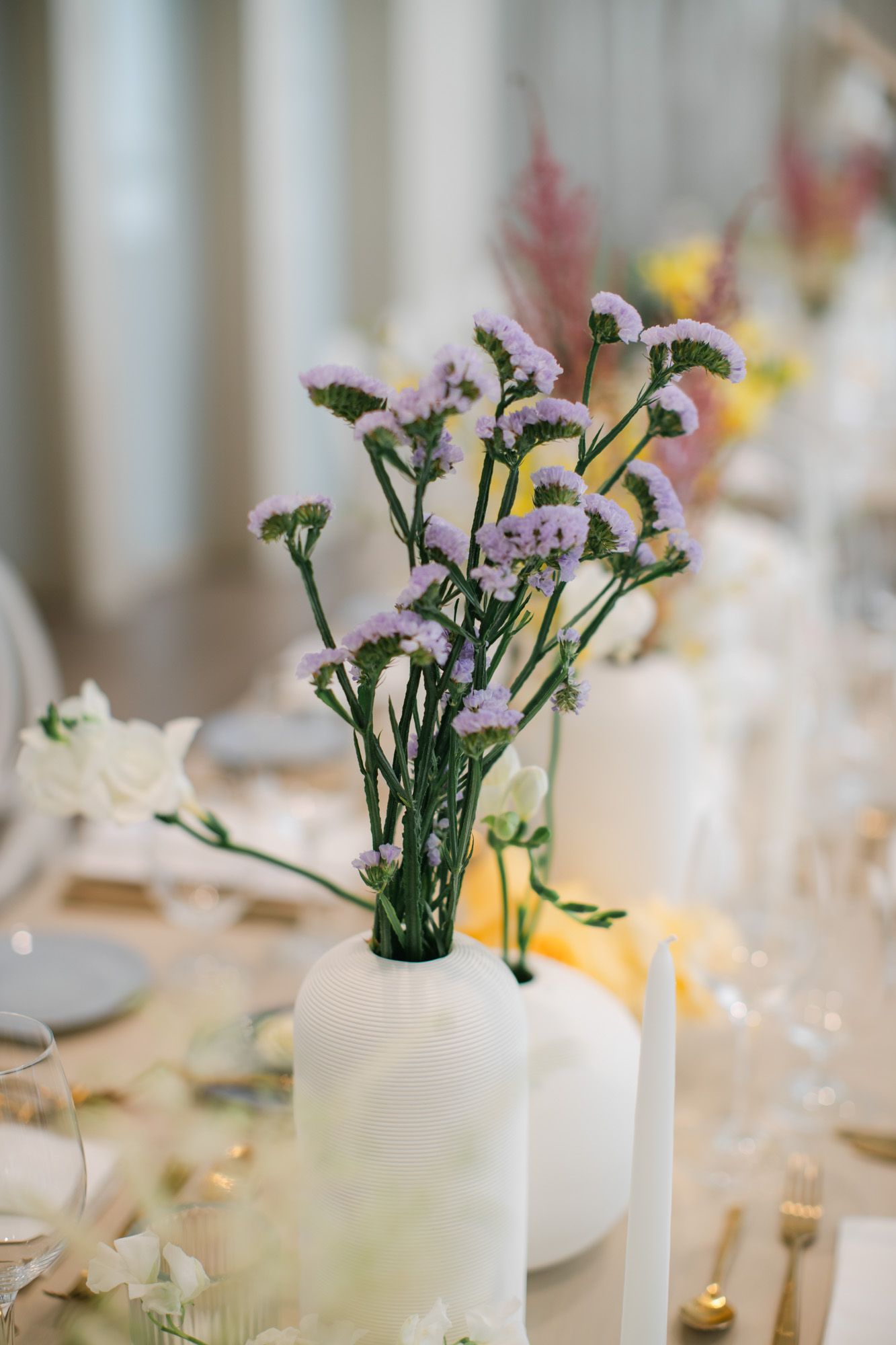Elegant wedding table centerpiece with lavender statice flowers in white vases with candles.