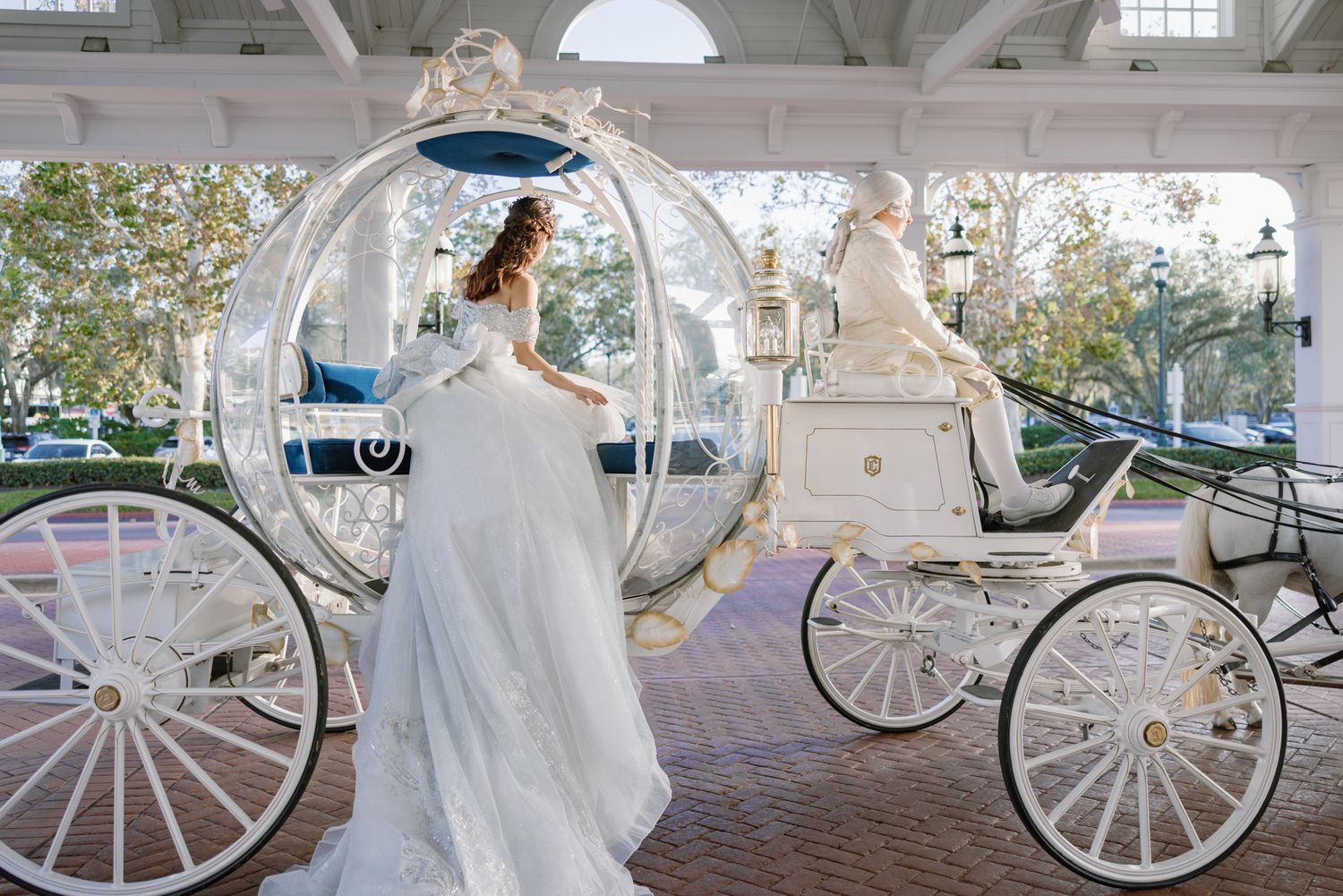 Bride in flowing white gown stepping into Cinderella's glass carriage at Walt Disney World.