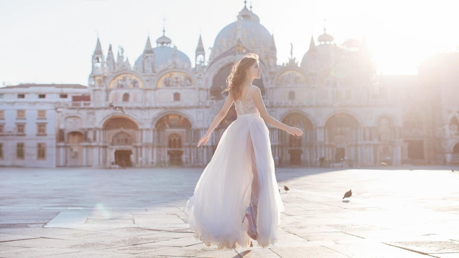 Bride in flowing white gown twirling at sunrise in St. Marks Square Venice.