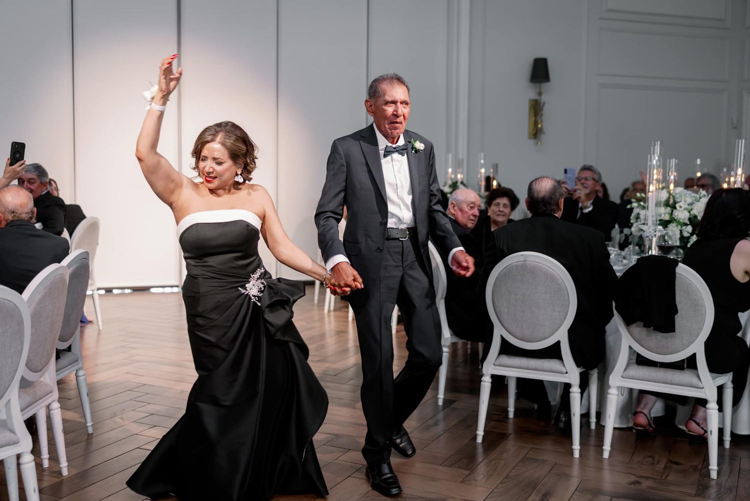 Couple in formal attire making a grand entrance at a wedding reception in an elegant white ballroom.