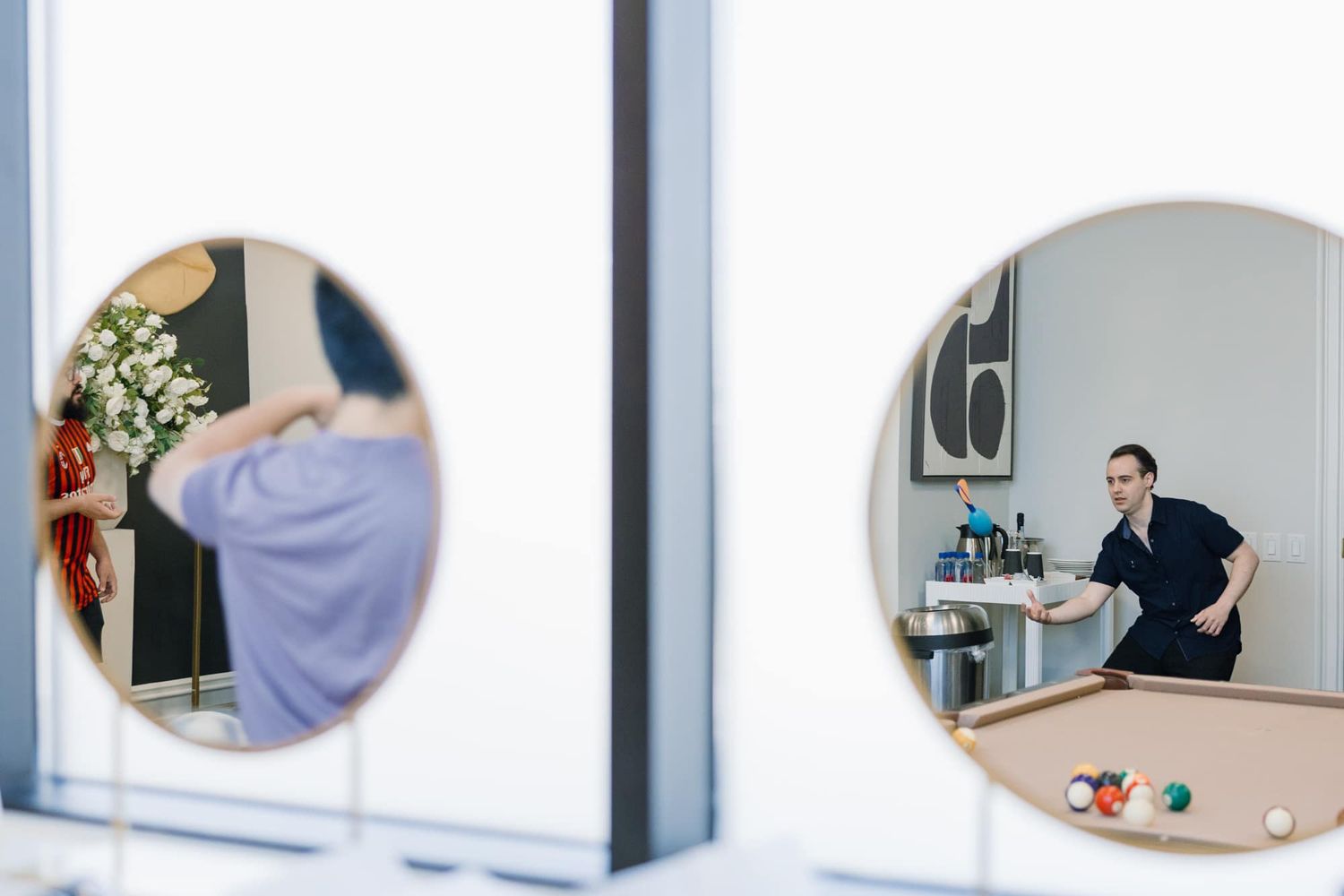 Two round mirrors reflecting a wedding preparation scene with a bride and stylist in a modern room.