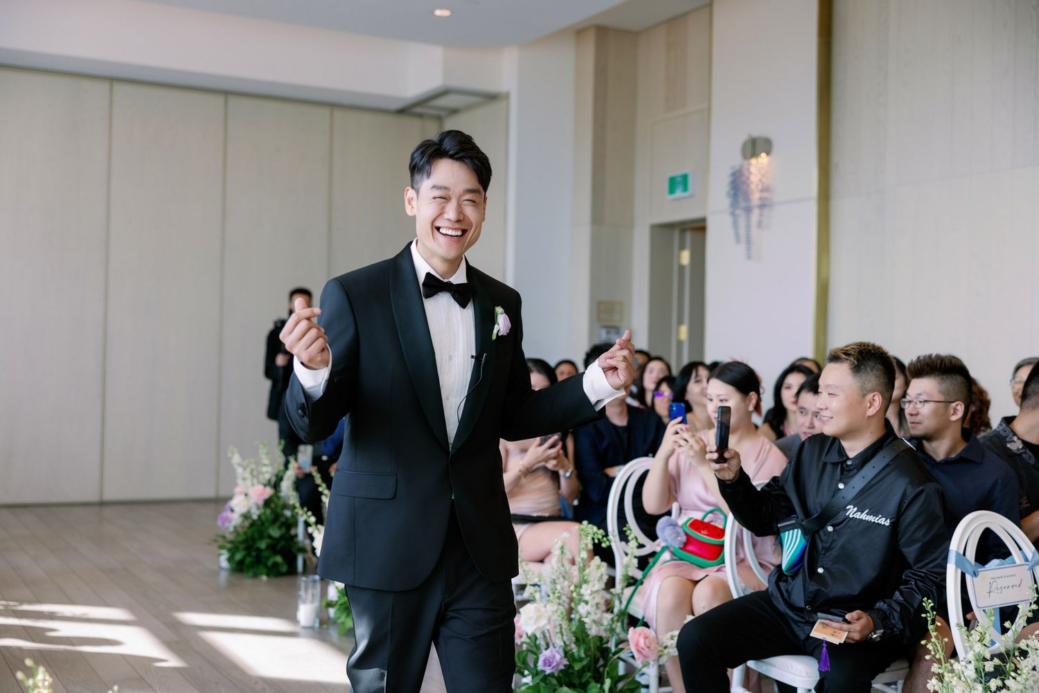 Handsome groom in black tuxedo smiling as he walks down the aisle at his wedding ceremony.
