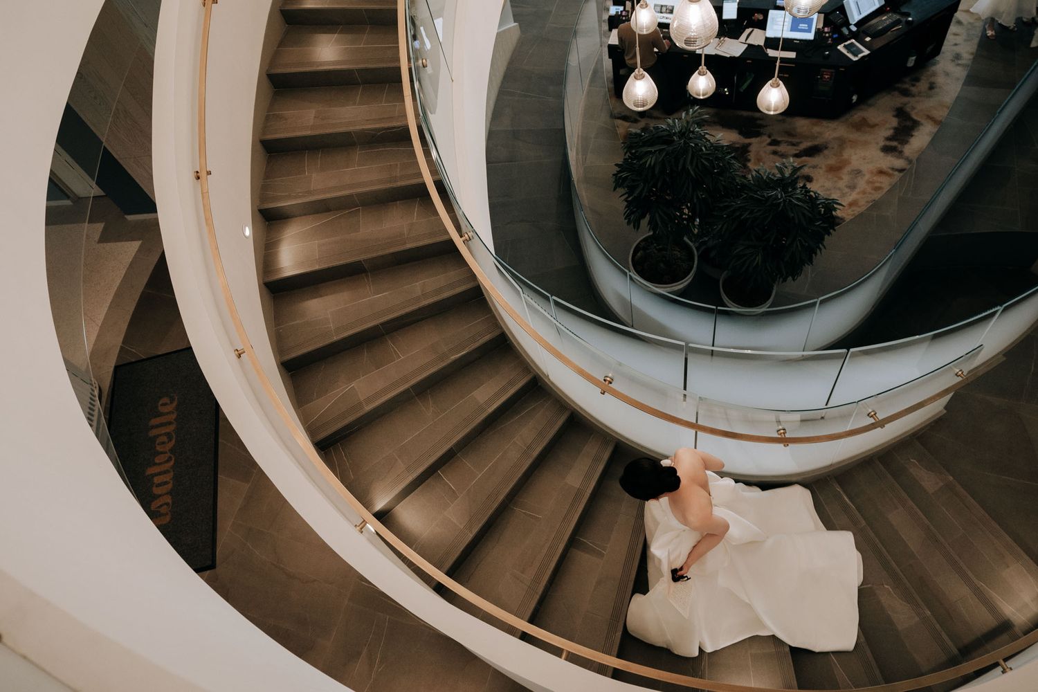 Aerial view of bride in white gown descending elegant spiral staircase in modern wedding venue.