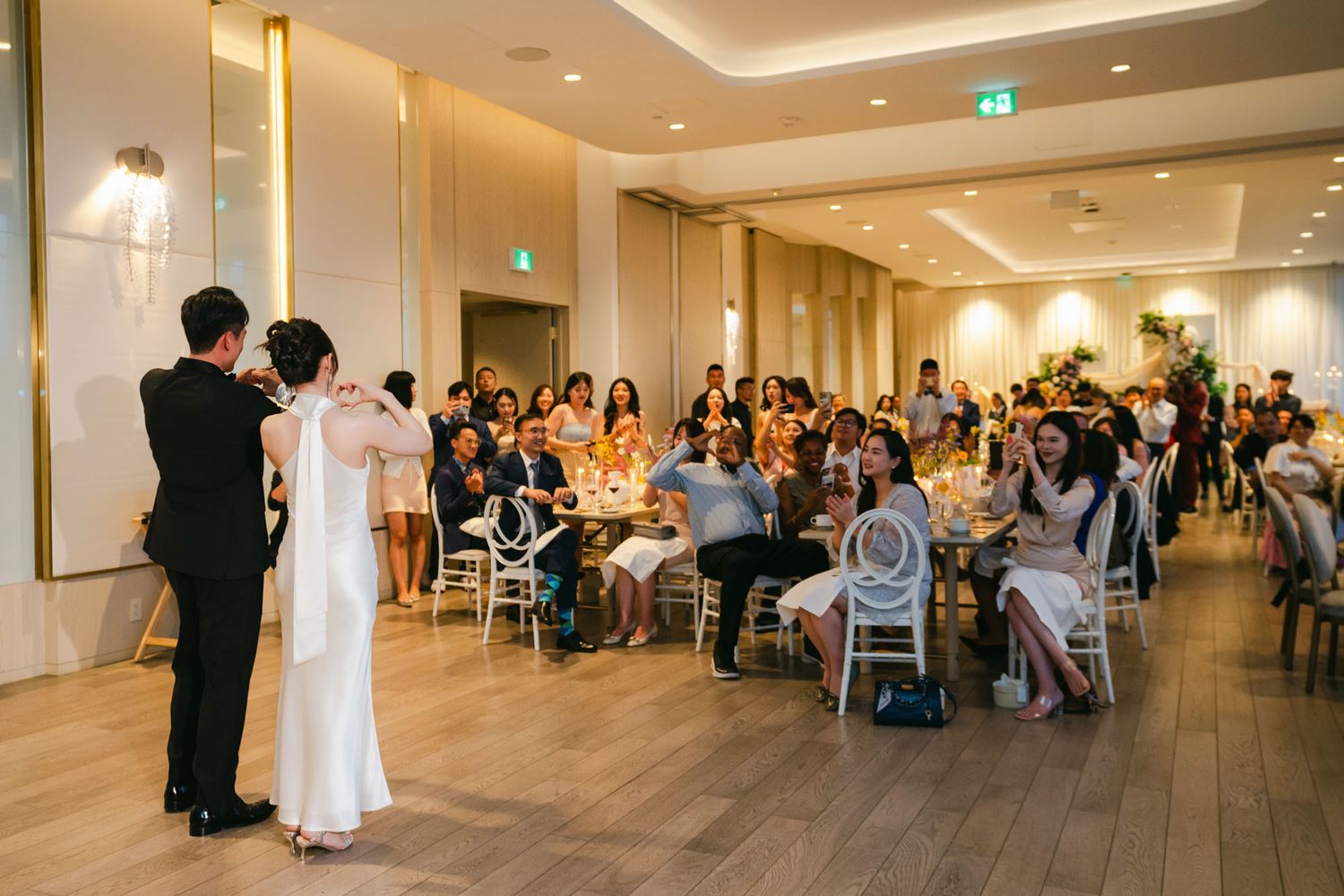 Groom twirls bride on the dance floor as smiling wedding guests watch from decorated reception tables.