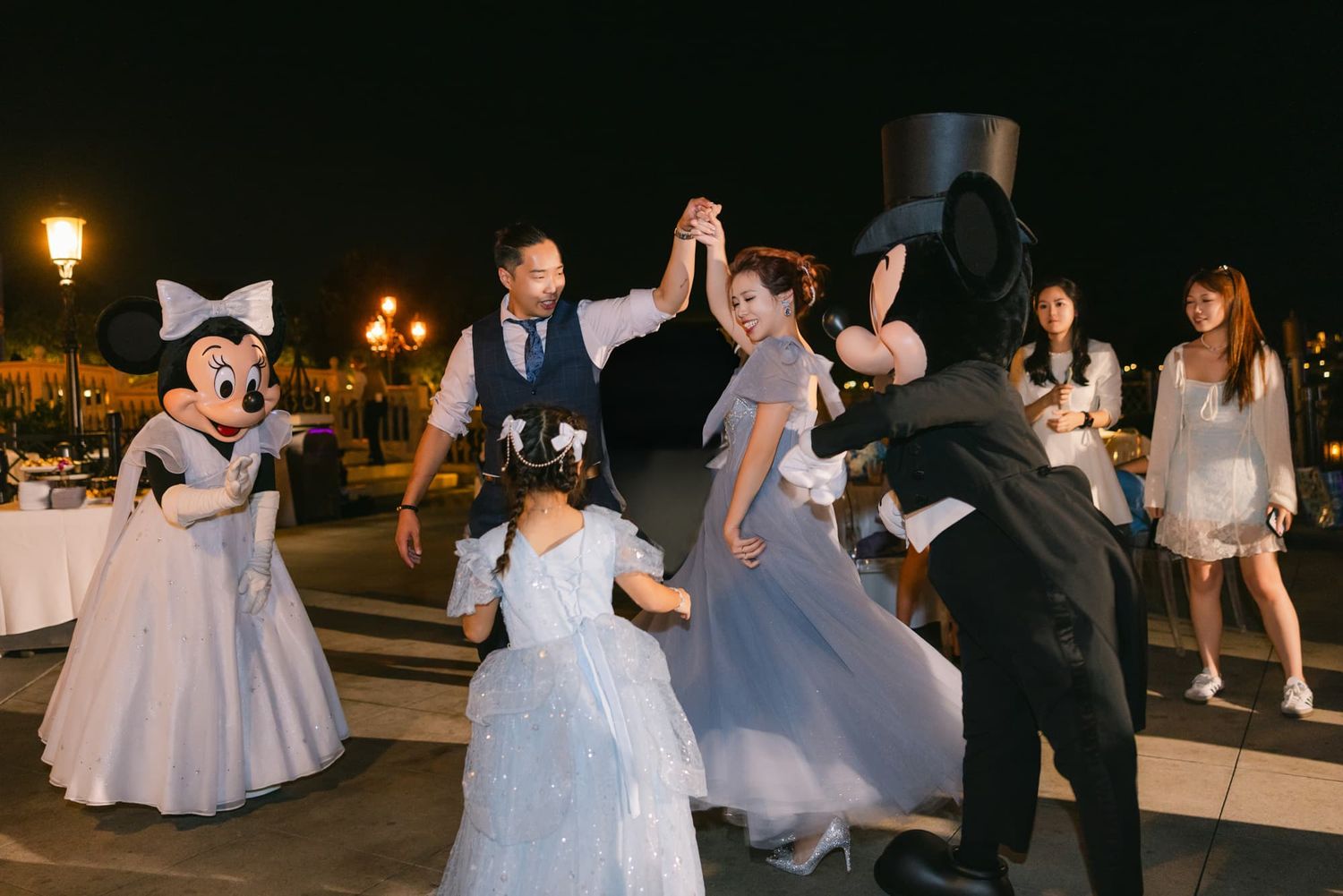 Couple dancing with Minnie Mouse and Mickey Mouse at a magical Disney wedding celebration outdoors at night.