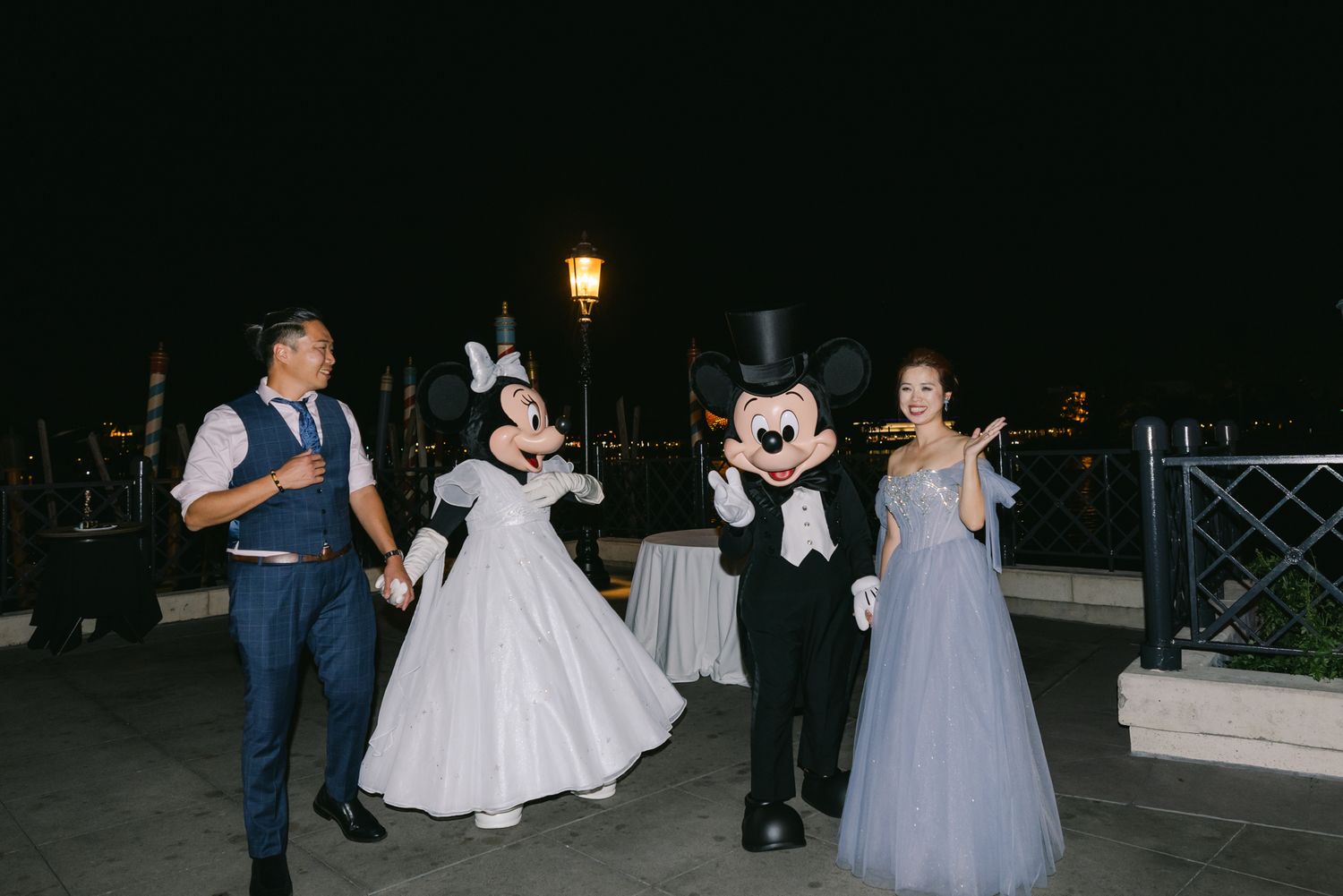 Newlyweds dancing with Mickey and Minnie Mouse characters in formal attire at a Disney World wedding.